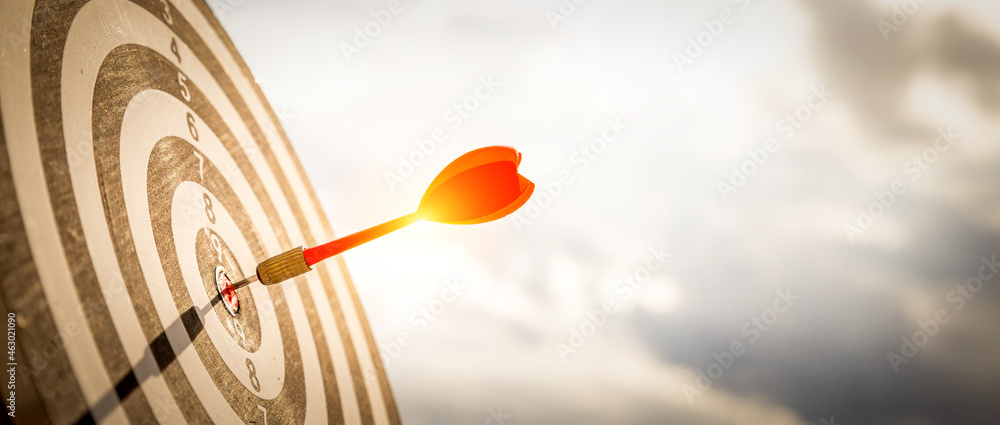 Close up shot red darts arrows in the target of dartboard center on dark blue sky background. Business target or goal success and winner concept. Close up shot red darts arrows in the target of dartboard center on dark blue sky background. Business target or goal success and winner concept.