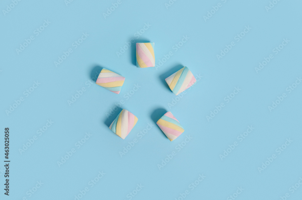 Fototapeta premium Flat lay food composition of colorful multi colored sweet sugary marshmallows laid out in the shape of five-pointed star on blue pastel colored background with copy space for advertising