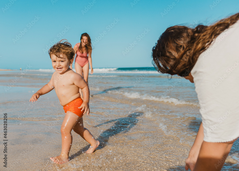 Cheerful son running near mothers on beach