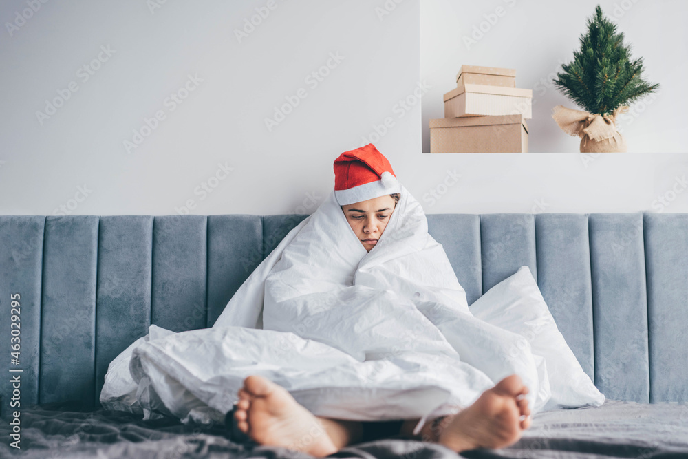  Wake up morning after party holidays. Woman in Santa hat under blanket in bed.