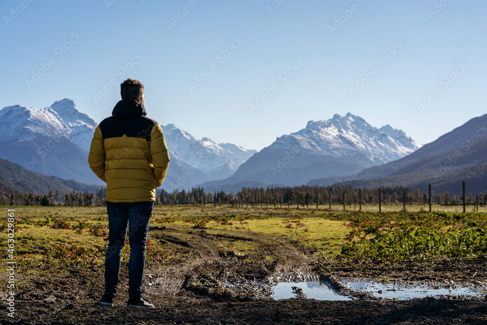 Young man on rural area with amazing view of snowy peak mountains. Glenorchy, New Zealand Young man on rural area with amazing view of snowy peak mountains. Glenorchy, New Zealand