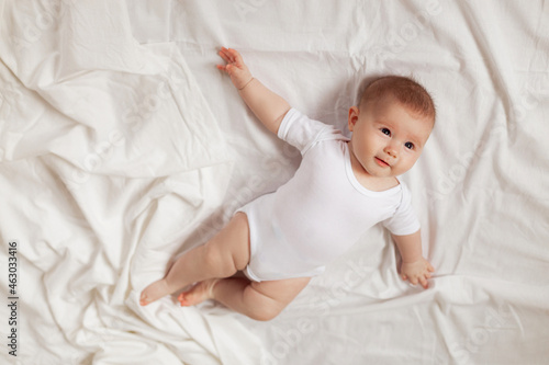 charming newborn baby in a white bodysuit lies on his back on a white fabric. top view. products for children. concept of happy childhood and motherhood. space for text. High quality photo photo