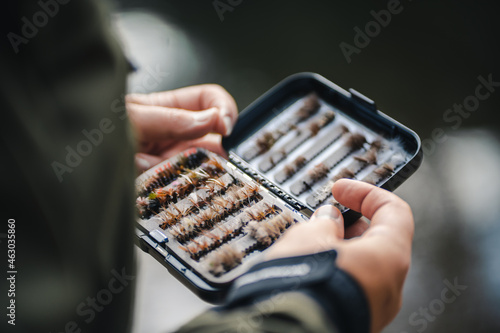 Fly fisherman chooses artificial flies from lures box for fly fishing at river. Blurry close up.