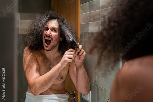 Young adult screaming in pain with afro hair is tangled in his comb shirtless