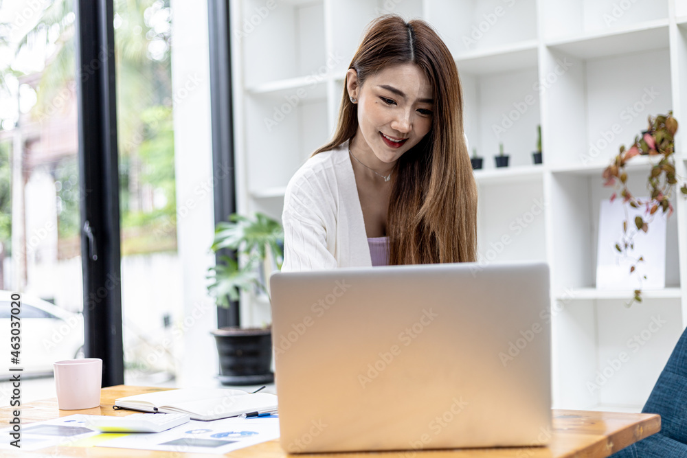 A beautiful Asian businesswoman standing in a room, she is talking business with her partner through a laptop messenger, she is a female executive of a startup company. Concept of financial management A beautiful Asian businesswoman standing in a room, she is talking business with her partner through a laptop messenger, she is a female executive of a startup company. Concept of financial management