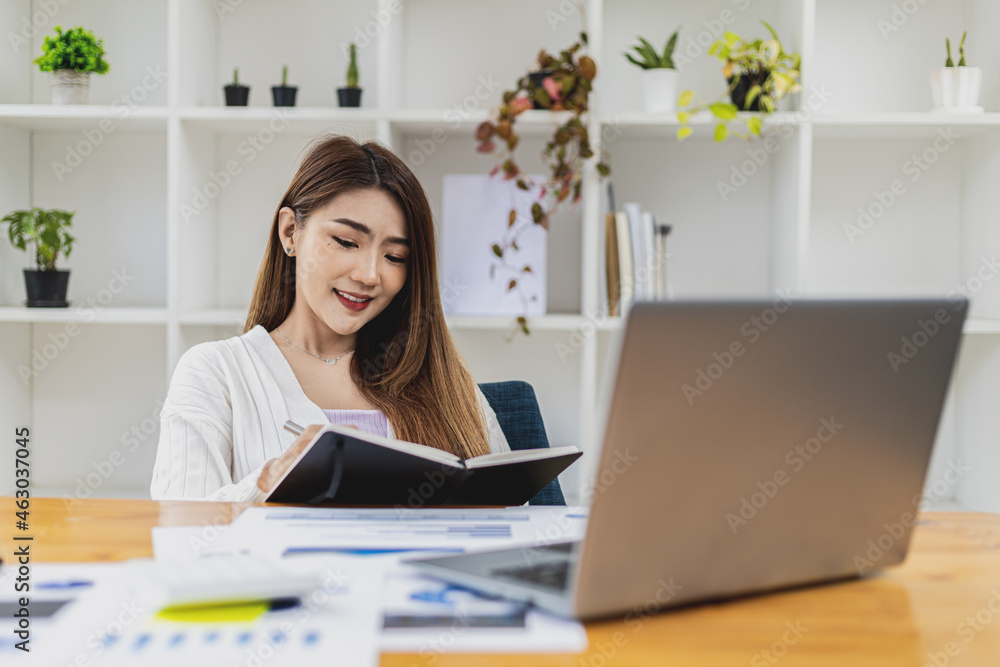 A beautiful Asian businesswoman working in the room, she is writing her schedule to remind herself in her notebook, she is a female executive of a startup company. Concept of financial management. A beautiful Asian businesswoman working in the room, she is writing her schedule to remind herself in her notebook, she is a female executive of a startup company. Concept of financial management.