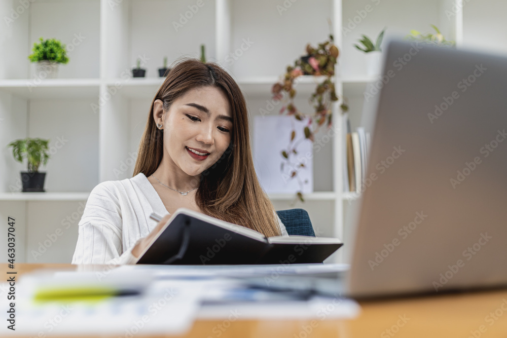 A beautiful Asian businesswoman working in the room, she is writing her schedule to remind herself in her notebook, she is a female executive of a startup company. Concept of financial management. A beautiful Asian businesswoman working in the room, she is writing her schedule to remind herself in her notebook, she is a female executive of a startup company. Concept of financial management.