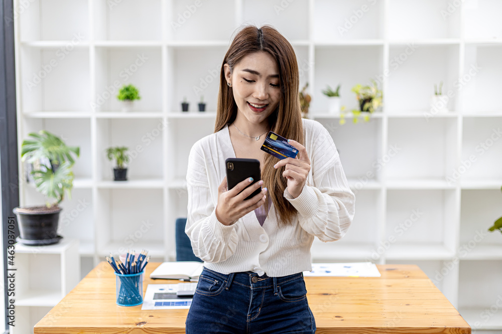 Beautiful Asian woman standing with smart phone and credit card, she fills in credit card information to pay for goods and services, online shopping concept pay by credit card and use via smartphone. Beautiful Asian woman standing with smart phone and credit card, she fills in credit card information to pay for goods and services, online shopping concept pay by credit card and use via smartphone.