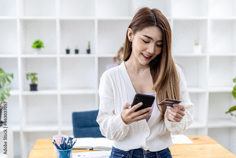 Beautiful Asian woman standing with smart phone and credit card, she fills in credit card information to pay for goods and services, online shopping concept pay by credit card and use via smartphone. Beautiful Asian woman standing with smart phone and credit card, she fills in credit card information to pay for goods and services, online shopping concept pay by credit card and use via smartphone.