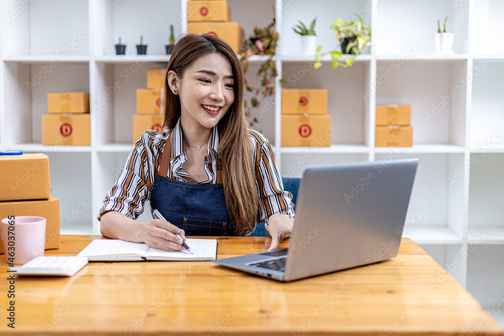 A beautiful Asian business owner opens an online store, she is checking orders from customers via laptop, sending goods through a courier company, concept of a woman opening an online business. A beautiful Asian business owner opens an online store, she is checking orders from customers via laptop, sending goods through a courier company, concept of a woman opening an online business.