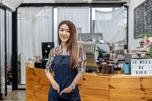 Portrait of a beautiful Asian woman in an apron standing in a coffee shop, she owns a coffee shop, the concept of a food and beverage business. Store management by a business woman.