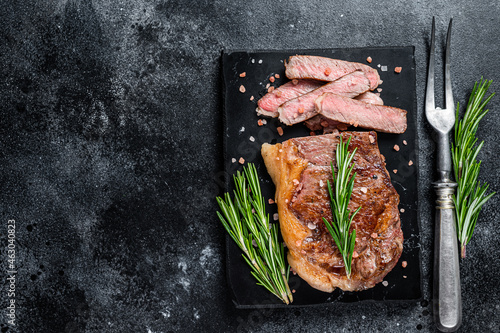 Cut roasted new york strip beef meat steak or striploin on a marble board. Black background. Top view. Copy space
