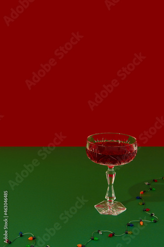 Christmas New Year creative composition with glass of red champagne and gerland on red and green background photo