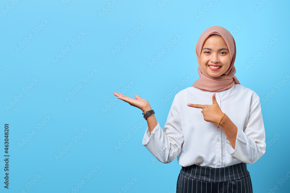 Portrait of smiling young Asian woman while presenting product and pointing with finger Portrait of smiling young Asian woman while presenting product and pointing with finger