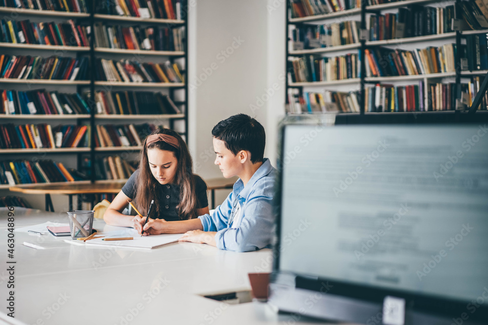 Teacher assisting girl with homework in library. Tutor working with middle school student. Teacher assisting girl with homework in library. Tutor working with middle school student.