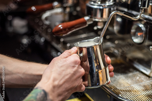 Closeup image of male hands pouring milk and preparing fresh cappuccino, coffee artist and preparation concept, morning coffee