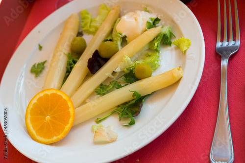 Delicious white asparagus sous vide garnished with hollandaise sauce, greens and orange