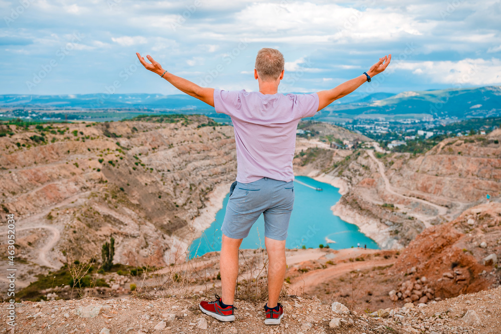 A young man stands at the Kadykovsky quarry in the shape of a heart with turquoise water in the Crimea. Famous tourist attraction, postcard view A young man stands at the Kadykovsky quarry in the shape of a heart with turquoise water in the Crimea. Famous tourist attraction, postcard view