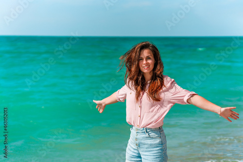 Portrait of a young woman in a shirt walking on the beach on a sunny day along the azure sea or ocean. The concept of summer holidays