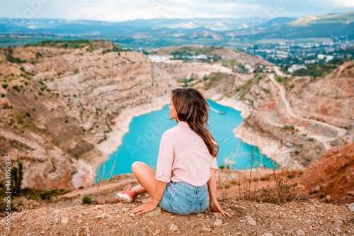 A young beautiful woman is sitting on the edge of a cliff with a Kadykovsky quarry in the shape of a heart in the Crimea. The concept of traveling in Russia