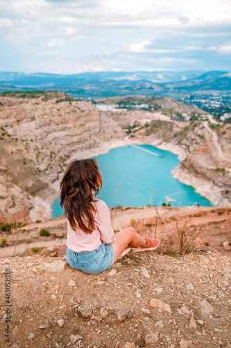 A young beautiful woman is sitting on the edge of a cliff with a Kadykovsky quarry in the shape of a heart in the Crimea. The concept of traveling in Russia photo