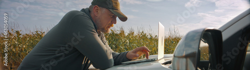 Canvas Print 50s Caucasian male farmer checking his laptop while having a sandwich outside ea