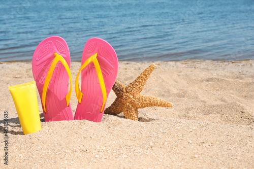Stylish flip flops, sun protection cream and starfish on sandy beach, space for text