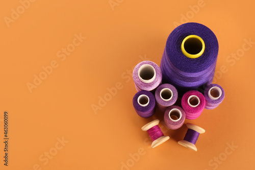 Different shades of violet and purple sewing threads on orange background, flat lay. Space for text