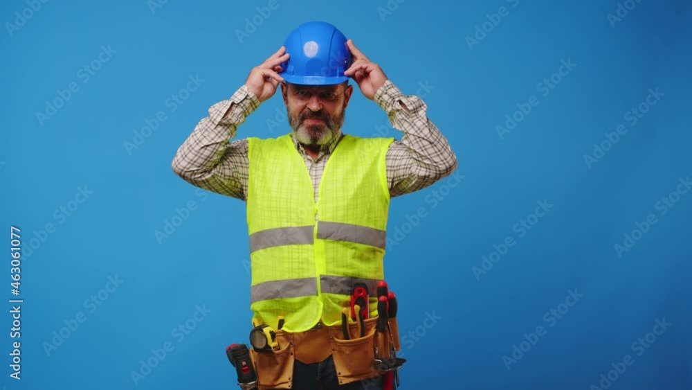 Smiling senior man builder in vest and hardhat against blue background Smiling senior man builder in vest and hardhat against blue background