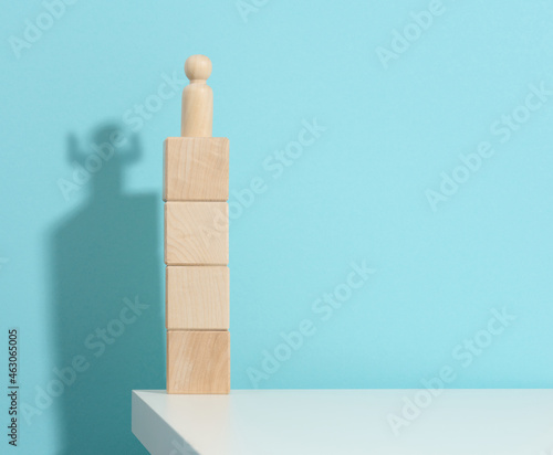 Fototapeta Naklejka Na Ścianę i Meble -  wooden figurine of a man stands high on the cubes, the shadow of a strong and victorious. Everyone is stronger than he thinks, a superhero. Blue background