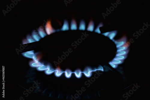 Hot blue small flame of gas burning on burner of kitchen stove at high oxygen level on dark background with lights off indoor
