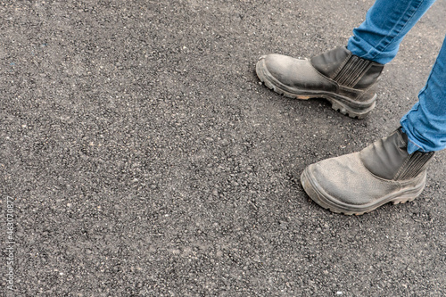 Foot of an unidentified person, wearing jeans and wearing a very worn and dusty boot, on a paved floor 