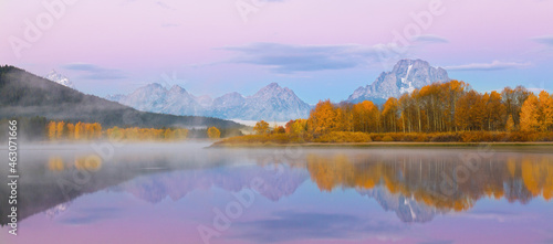 Dawn image of the snowcapped Grand Tetons with mist, orange fall colors and perfect reflections in the river.