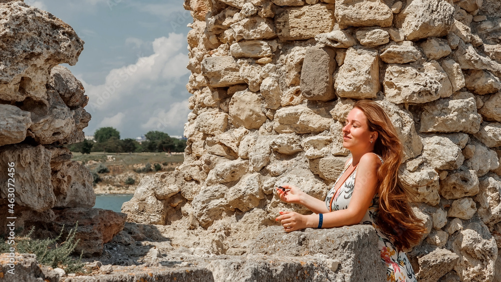 Fototapeta premium A girl in a dress travels to the ancient ruins of the fortress. Tourism in Crimea.