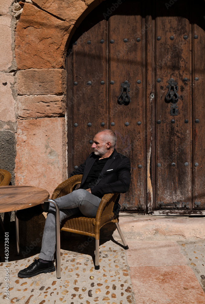 Portrait of adult man sitting on outdoor chair against old wooden door Portrait of adult man sitting on outdoor chair against old wooden door