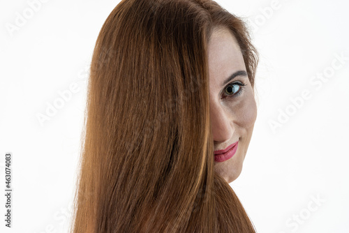 Portrait of a middle-aged woman with long brown healthy hair, natural skin with wrinkles near green eyes. Light background. Caring for beauty and women's health concept