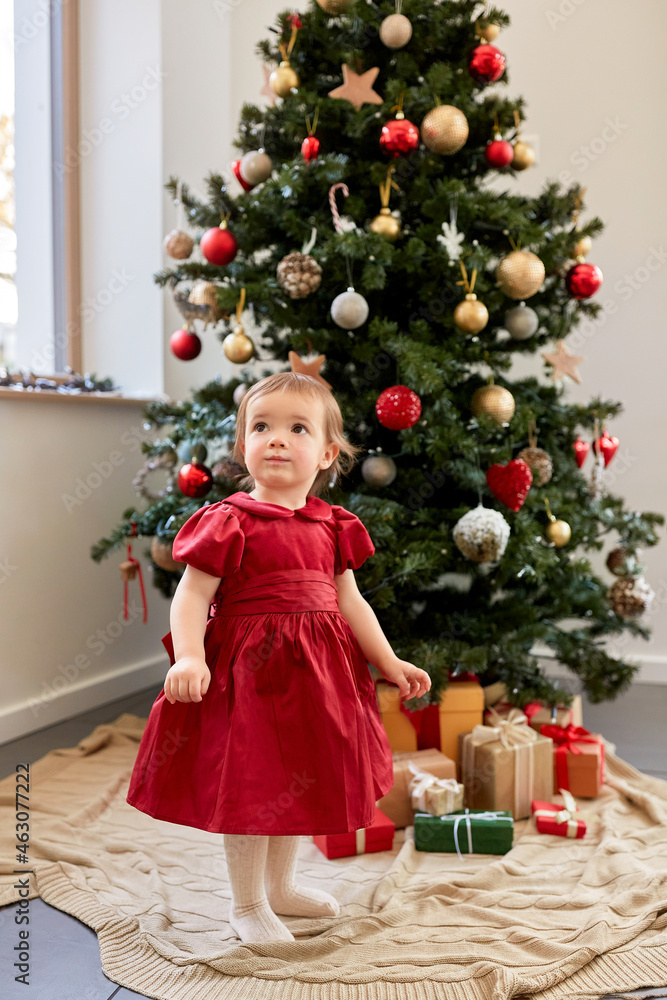 winter holidays and childhood concept - lovely baby girl in red dress over christmas tree at home winter holidays and childhood concept - lovely baby girl in red dress over christmas tree at home