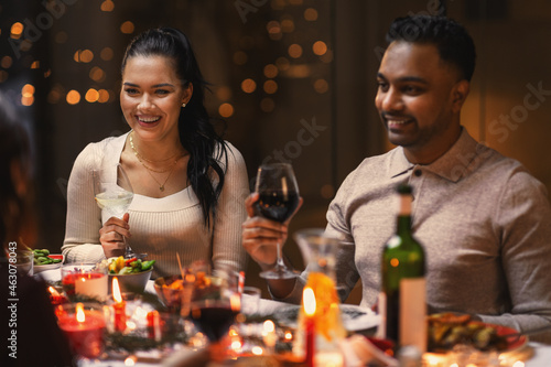 holidays  party and celebration concept - multiethnic group of happy friends having christmas dinner at home and drinking wine