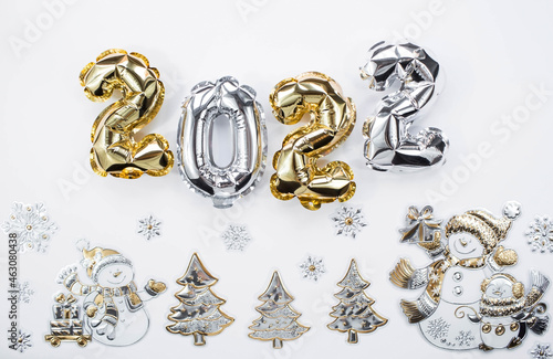 Banner. Happy New Year and Merry Christmas. Balloons made of gold and silver foil with the number 2022 and snowmen on a white background. Flat lay.