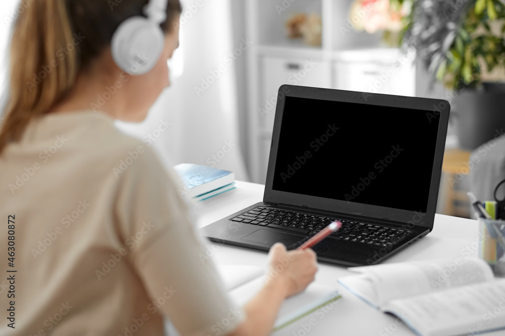education, online school and distant learning concept - student woman in headphones with laptop computer, notebook and book at home education, online school and distant learning concept - student woman in headphones with laptop computer, notebook and book at home