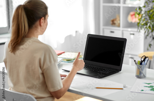 education, online school and distant learning concept - student woman with laptop computer and pencil drawing showing thumbs up at home