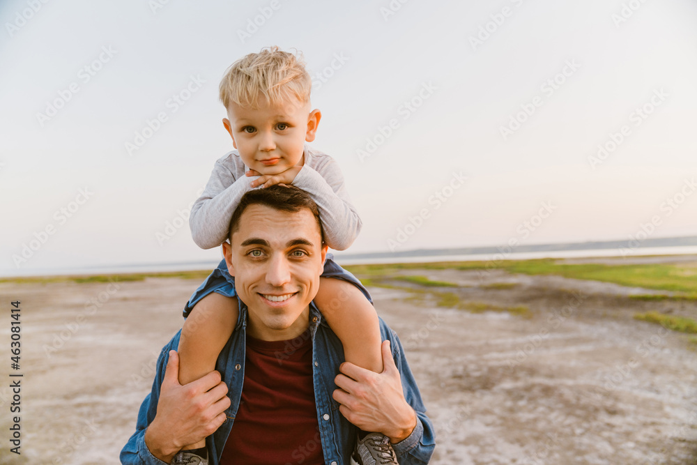 Young father carrying son on his shoulders while walking outdoors Young father carrying son on his shoulders while walking outdoors