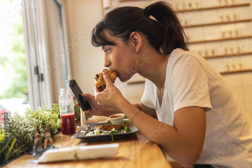 Teenage girl sitting in fast food restaurant eating burger and drinks fresh organic juice. 
