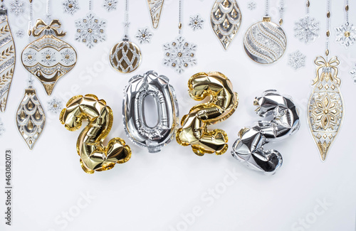 Banner. Happy New Year and Merry Christmas. Balloons made of gold and silver foil with the number 2022, snowflakes, garland and Christmas tree balls on a white background. Flat lay.
