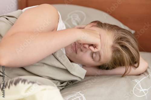 A teenage girl rubs her eyes with her hand, waking up in her bed. Close-up. Daily routine, early rise,  awakening concept