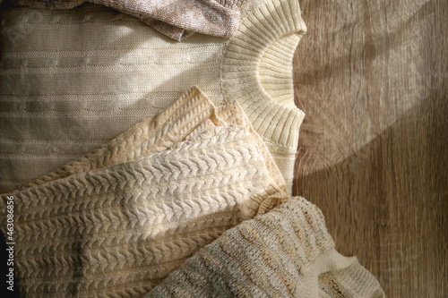 White and beige sweaters on wooden background, illuminated by sunlight. Flat lay.