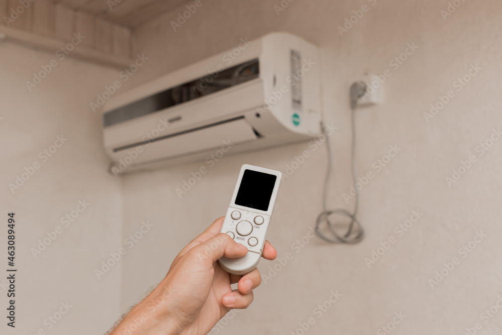 The guy's hand holds the remote control of the air conditioner. Cooling and temperature control in the room of the house The guy's hand holds the remote control of the air conditioner. Cooling and temperature control in the room of the house