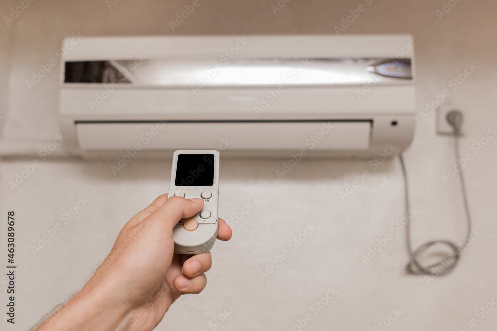 The guy's hand holds the remote control of the air conditioner. Cooling and temperature control in the room of the house The guy's hand holds the remote control of the air conditioner. Cooling and temperature control in the room of the house