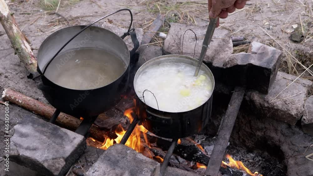 Male Preparing Food in a Saucepan on a Bonfire in Woods Outdoors. Male