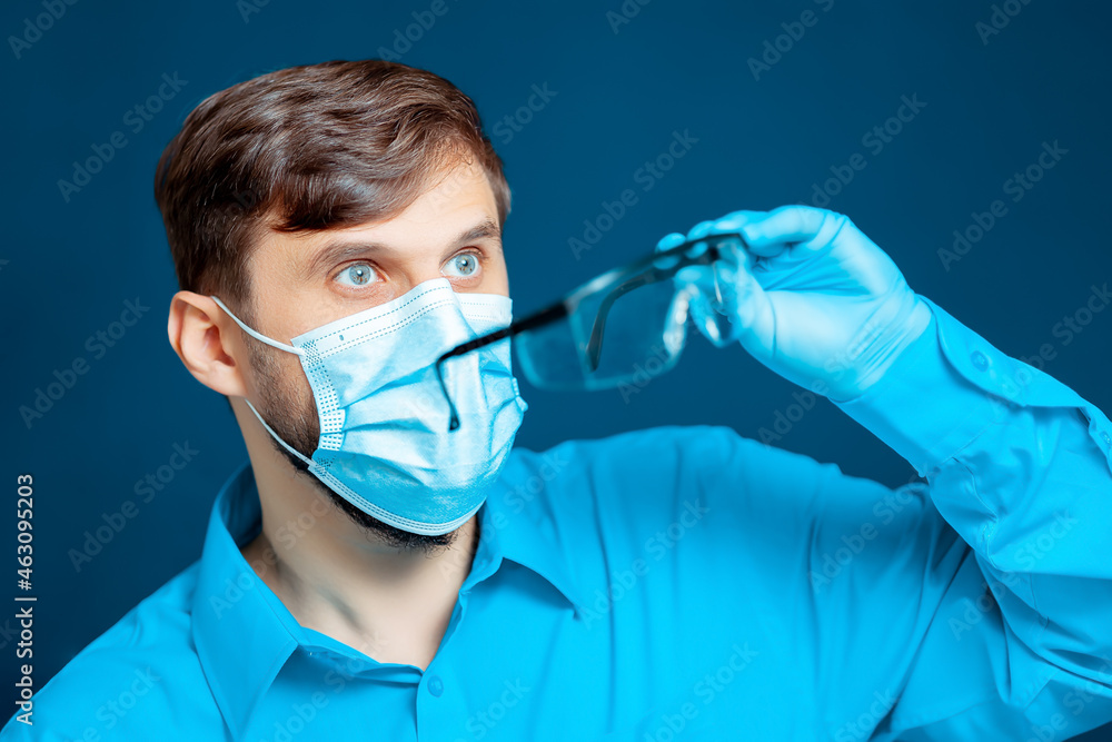 doctor wearing a protective mask and gloves puts on medical glasses. doctor wearing a protective mask and gloves puts on medical glasses.